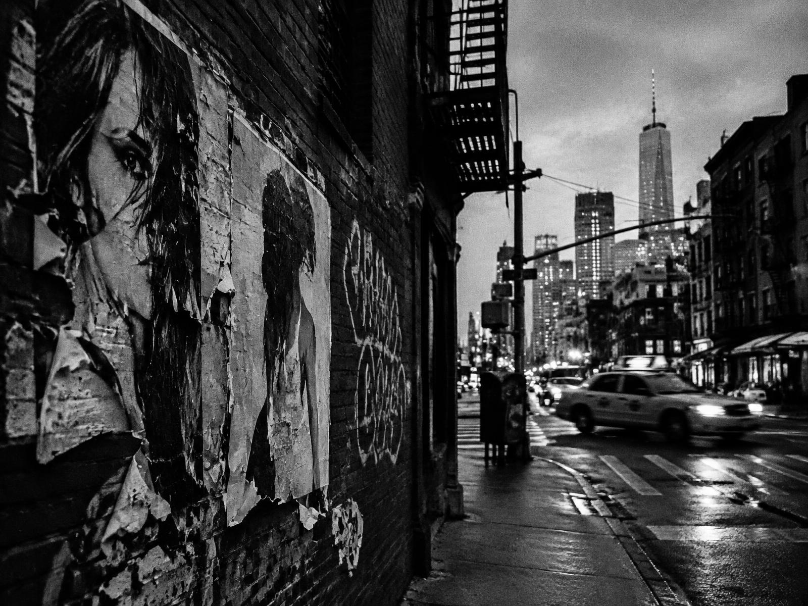Wheatpasted posters and graffiti on a Lower Manhattan street corner at dusk